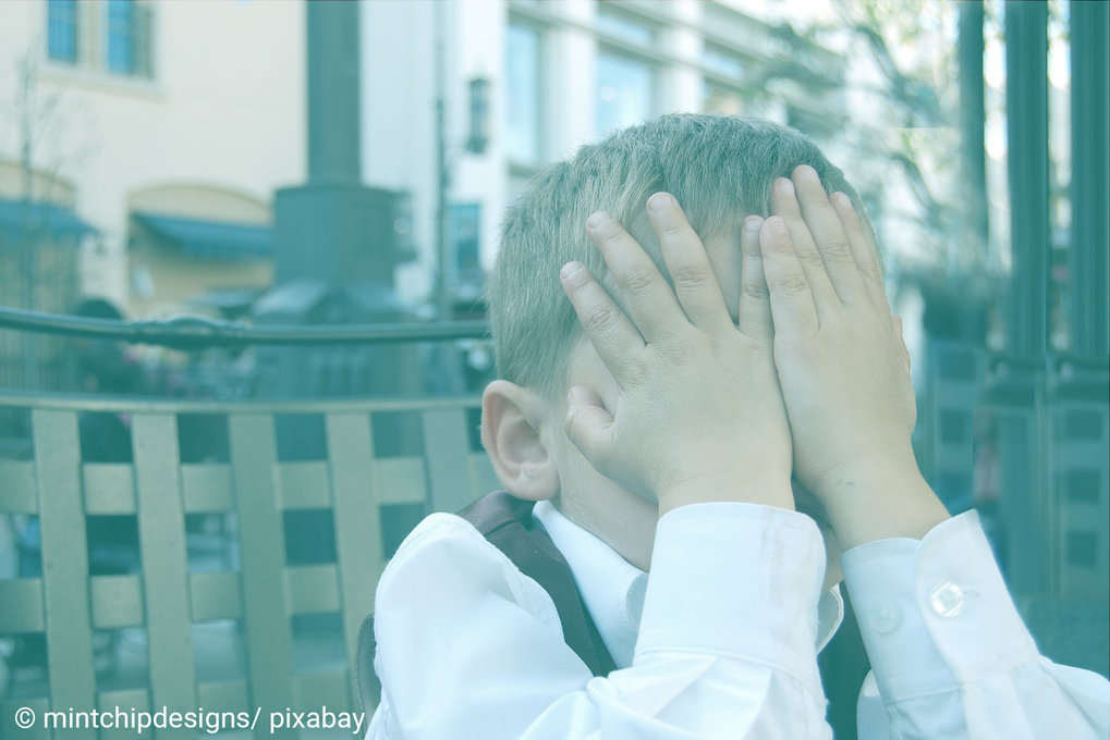 A little boy covers his face with his hands.