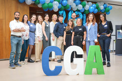 Group stands behind large CGA letters, balloons overhead.