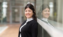 Woman in a black cardigan standing against a glass wall, reflection visible.